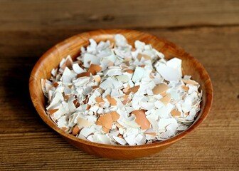 Crushed egg shells in a bowl on the wood table. Eggshells can be used in the kitchen and garden.