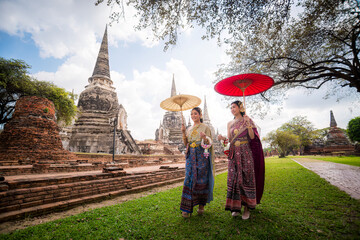 Asian beautiful wearing Thai traditional dress holding umbrella in ancient temple with old pagoda...