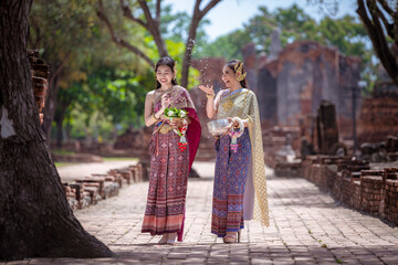 Beautiful Asian woman wearing Thai dress traditional pose happiness to playing splash water during Songkran festival is funny festival traditional holiday in Thailand .