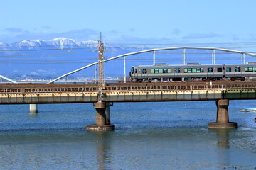 冠雪した蓬莱山を背景に、瀬田川の鉄橋を渡る電車