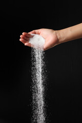 Hand sprinkling sugar on black background