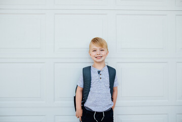 Young boy standing in front of garage with backpack before school.