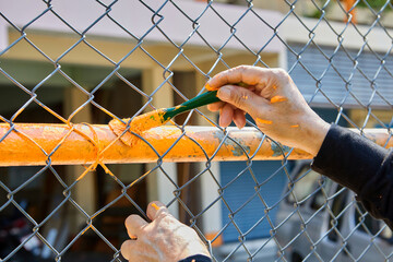 Cropped hand of man painting orange color on chainlink fence