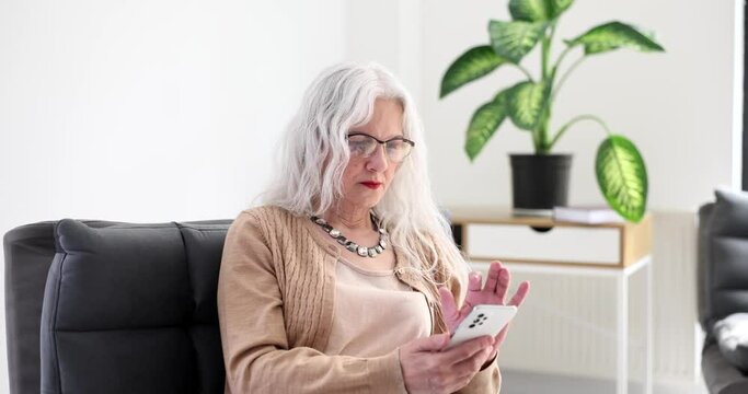 Elderly woman with gray hair in eyeglasses dialing mobile phone number at home 4k movie slow motion. Call parents concept