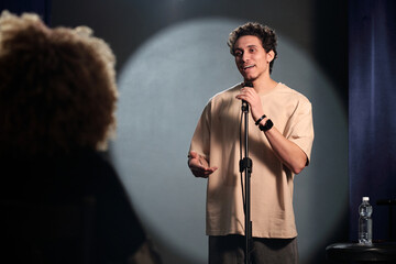 Young stand up comedian, actor or showman standing on stage in front of audience during monologue...