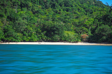 Aerial panorama of Thailand's verdant, lush tropical island, National Park Island, with blue and aquamarine the sea, and clouds shining by sunlight in the background.