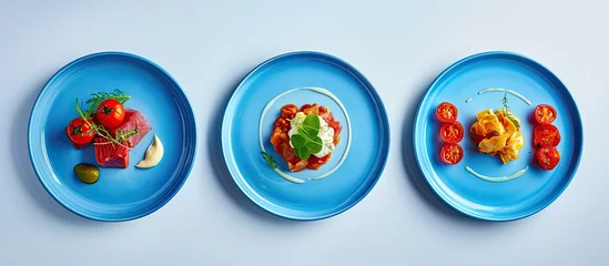 Fensteraufkleber Three blue plates are elegantly displayed on a crisp white background, each showcasing a different mouthwatering dish. The assortment of food ranges from appetizers to main courses, creating a © 2rogan