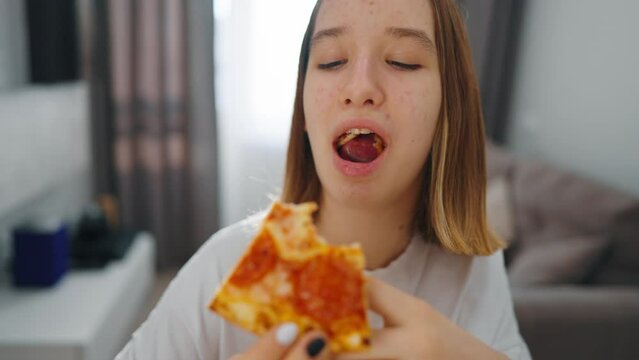 Close up little girl eating pizza food. Hungry happy young female is eating piece of pizza, taking a bite from pizza indoor at home in a pizzeria. Fast food, children unhealthy tasty food concept.