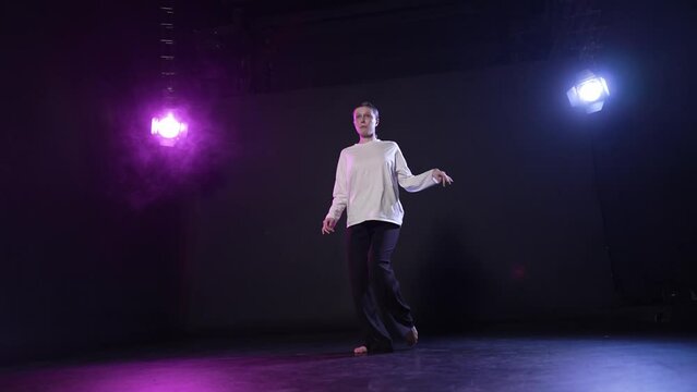 Young woman performing dance in studio. Expression girl dancing elegant contemporary in dance darkness studio in multi-colored violet spotlights. Motion dance, female professional dancer concept.