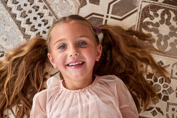 Joyful girl with blue eyes lies on floor dreaming about future and looking at camera. Positive...