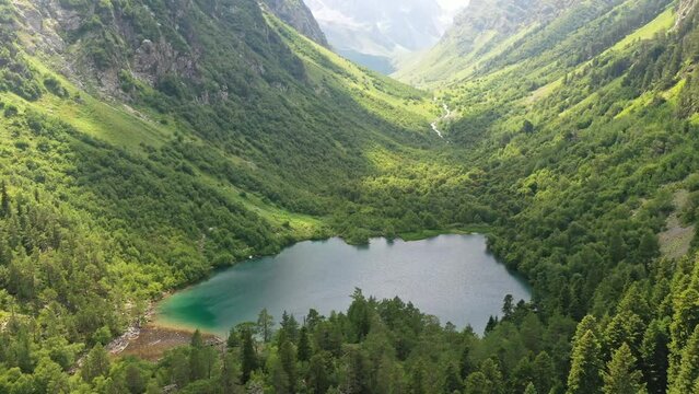Flying over a forest and lake with turquoise water among the mountains in sunny weather. Ahead is a green valley between the mountains. 4K.