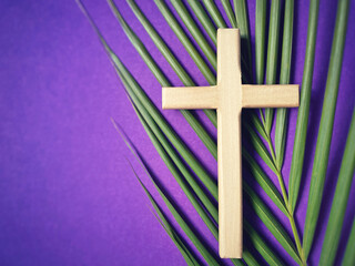 Holy Week, Lent, Palm Sunday, Good Friday, Easter Sunday Concept. Wooden cross with palm leaf in purple background with copy space.
