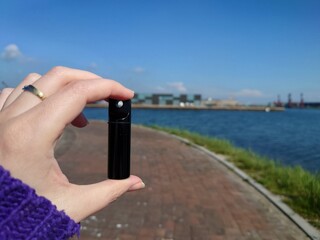A woman's hand holding a geocache that looks like a tiny black container which was hidden on a street, found during a sunny day in Netherlands © Eva