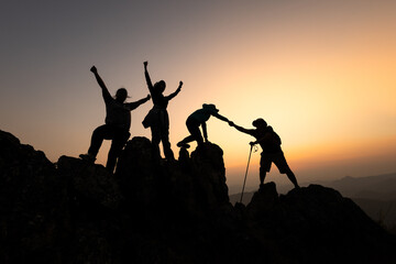 Silhouette of Group team tourists lends helping hand climb cliffs mountains helping hand. teamwork people climbers climb top overcoming hardships, teamwork helping hand business travel  concept.