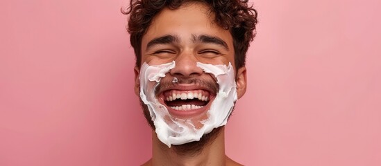 A man smiles while shaving his face for a headshot photo. He holds a razor to his cheek, focusing on grooming and personal care. - obrazy, fototapety, plakaty
