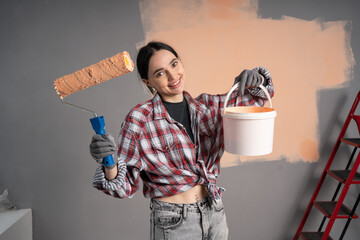Portrait on female painter showing bucket and painting roller on the camera. Woman renovation her...