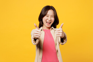 Young excited woman of Asian ethnicity she wear pink t-shirt beige shirt pastel casual clothes showing thumb up like gesture look camera isolated on plain yellow background studio. Lifestyle portrait.