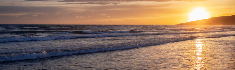 Web banner 4x1. A series of low rolling waves runs over the sandy beach. A sunny path