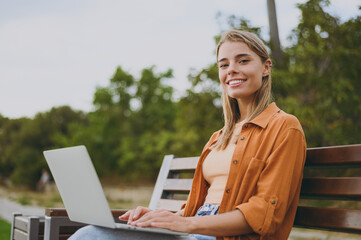 Young IT woman she wearing orange shirt casual clothes hold use work on laptop pc computer sit on...