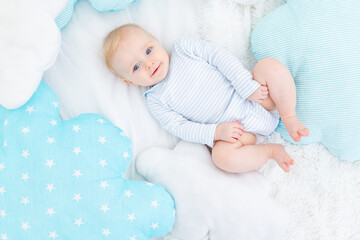 baby boy six months old lying on a bed with soft blue pillows, smiling blonde baby