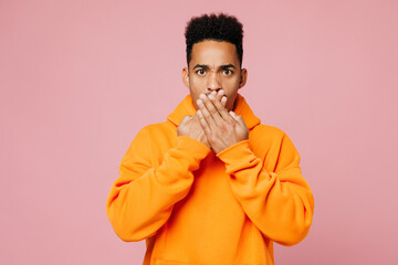 Young sad mad man of African American ethnicity he wear yellow hoody casual clothes cover mouth with hands look camera isolated on plain pastel light pink background studio portrait Lifestyle concept