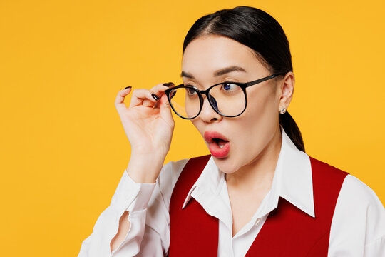 Close up young shocked corporate lawyer employee business woman of Asian ethnicity wearing formal red vest shirt work at office look aside on area isolated on plain yellow background. Career concept.