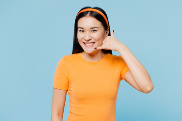 Young happy woman of Asian ethnicity she wears orange t-shirt casual clothes doing phone gesture like says call me back isolated on plain pastel light blue cyan background studio. Lifestyle concept.
