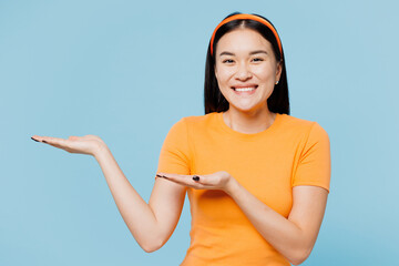 Young smiling happy woman of Asian ethnicity wear orange t-shirt casual clothes point hands arms...