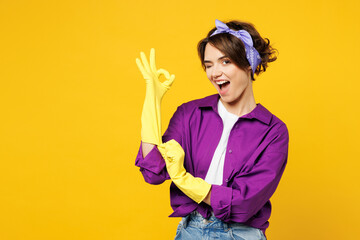 Young cheerful fun smiling woman wears purple shirt rubber gloves while doing housework tidy up...