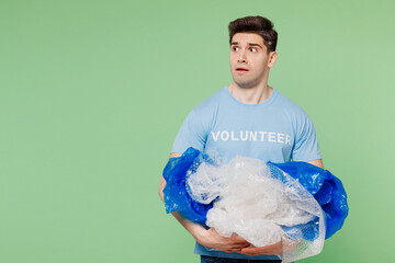 Young shocked sad man wear blue t-shirt white title volunteer hold pile of polyethylene film look...