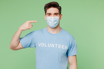 Young man wear blue t-shirt white title volunteer point on protective disposable mask look camera isolated on plain pastel green background. Voluntary free work assistance help charity grace concept.