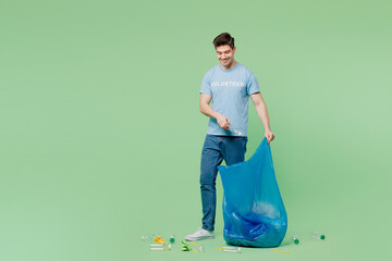 Full body young man wear blue t-shirt title volunteer hold big plastic bag pick up rubbish clean...