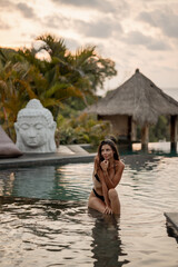 Young pretty tourist woman sitting in the swimming pool with tropical balinese landscape.  Summer vacation on Bali island