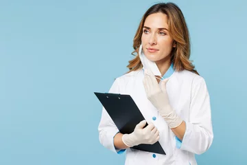  Female doctor woman wears white medical gown suit work in hospital clinic office hold clipboard with documents look aside take off mask isolated on plain blue background. Health care medicine concept. © ViDi Studio