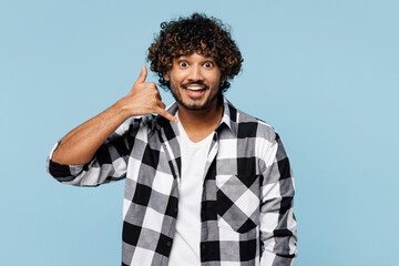 Young smiling Indian man he wears shirt white t-shirt casual clothes doing phone gesture like says call me back isolated on plain pastel light blue cyan background studio portrait. Lifestyle concept.