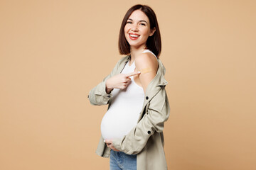 Side view young pregnant woman future mom wear grey shirt point on vaccine adhesive plaster with belly stomach tummy with baby isolated on plain beige background. Maternity family pregnancy concept.