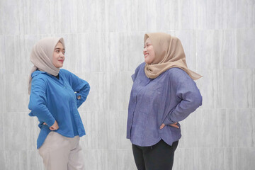 Two Asian Indonesian women wearing hijabs wearing light blue and dark blue clothes