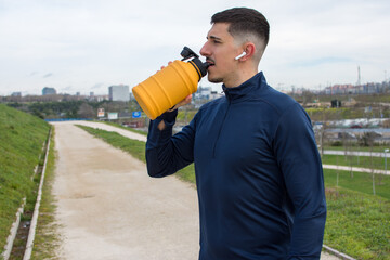 Fitness man taking a break drinking water from a yellow bottle