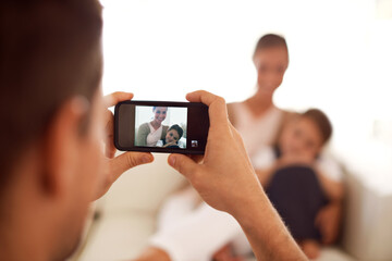 Father taking a picture of family, home and screen with smartphone and social media in a lounge. Parents, mother and dad with daughter or child with memory and mobile user with digital app or network