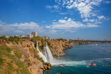 Fototapeta premium The moment when the Lower Düden waterfall flows into the sea, against the background of the steep shores of the Mediterranean and the urban development of the city of Antalya.