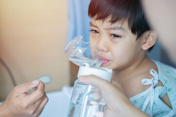 Shot view of little sick Asian boy is crying while drink water from a bottle in hospital room.