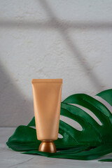 Plastic tube for cream or lotion. Skin care or sunscreen cosmetic with stylish props on tropical monstera leaves background