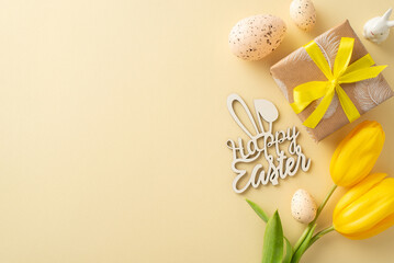 Charming Easter setup concept. Overhead view of kraft paper wrapped gift, yellow tulips, Happy easter greeting, Easter hare figurine, quail eggs, arranged on a light beige surface with space for copy