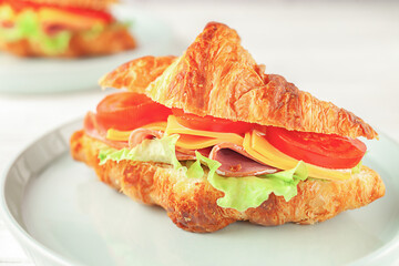 Fresh croissant with ham and lettuce on white wooden background