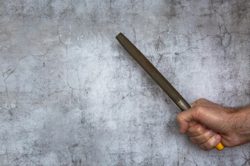 A man's hand holds a file against the background of a concrete wall. The concept of repair work.