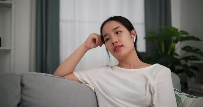 Footage selective focus shot, Relaxed young woman wear wireless headphones enjoying rest sitting on sofa in living room listening to music at home