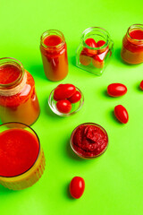 Small glass bottles of fresh tomatoes juice, cherry tomatoes, tomato paste on a green background. Healthy food.