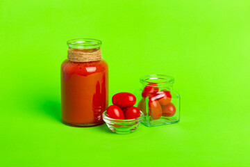A small glass bottle of fresh tomatoes juice, cherry tomatoes on a green background.