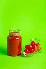 A small glass bottle of fresh tomatoes juice, cherry tomatoes on a green background.