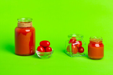 Small glass bottles of fresh tomatoes juice, cherry tomatoes on a green background.